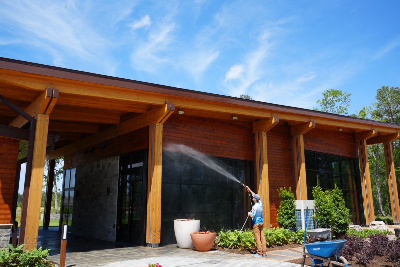 Technician soft washing the exterior of a modern wood and stone building in The Woodlands, TX