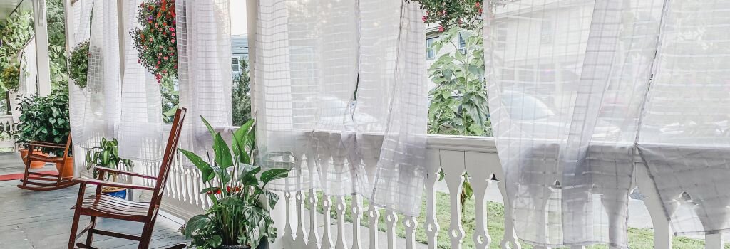 A serene front porch with a wooden rocking chair and sheer curtains in the breeze, evoking the quiet peace of a home that has served its purpose well