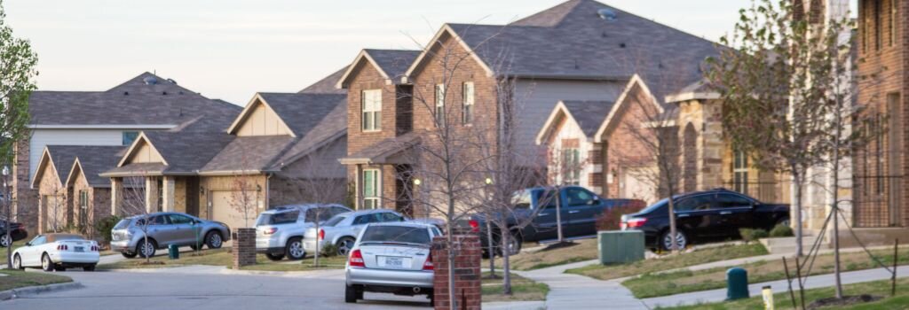 A well-kept residential Houston neighborhood street at dusk showing brick homes with maintained lawns and driveways