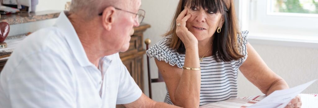 An older couple reviewing documents together at home, the woman's expression showing careful concern as they work through an important decision