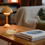 home with cozy-interior-with-wooden-table-and-lamp with picture window behind couch. Focus is on books and table in foreground.