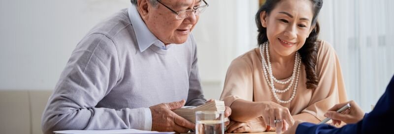 An older couple reviewing documents together at the kitchen table, considering their options for the family home