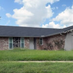 a house in southwest houston with heavily overgrown grass in front yard on a sunny day