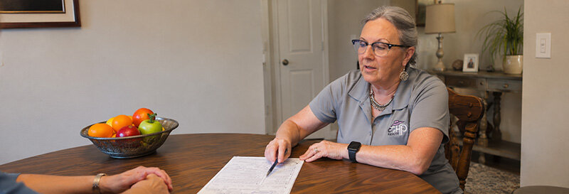 Homeowner signing paperwork at a kitchen table with Becky explaining details