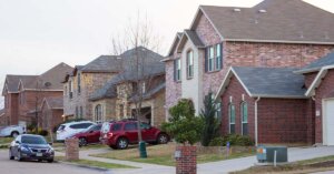 Quiet Houston-area house exterior at sunset, cars in driveways one facing foreclosure