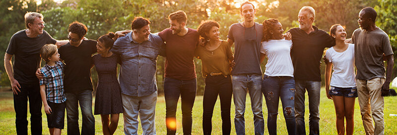group of siblings and their significant others as parr of a large family in a park with a setting sun behind them locked arms around their shoulders