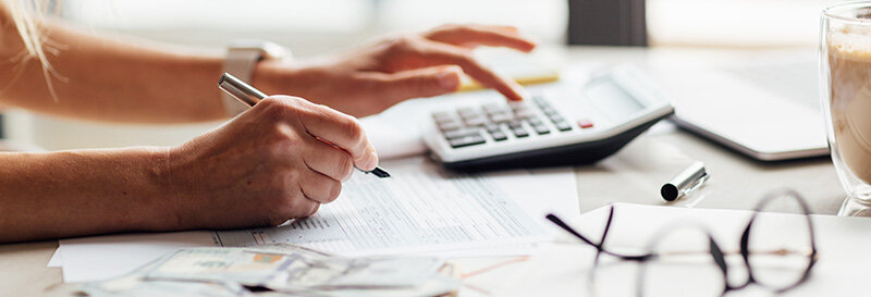 Calculator and appraiser preparing a report on a kitchen table with a coffee mug and glasses