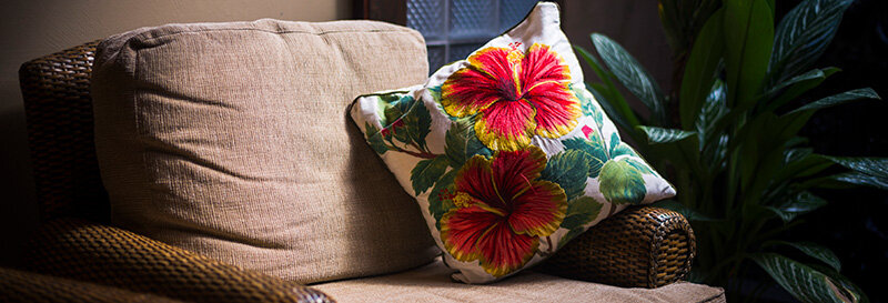 Empty armchair by a sunlit window with a folded blanket, quiet interior, and pillow on armrest