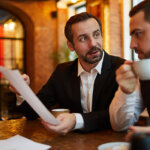 Two brothers sitting together in conversation in a restaurant, one with coffee cup