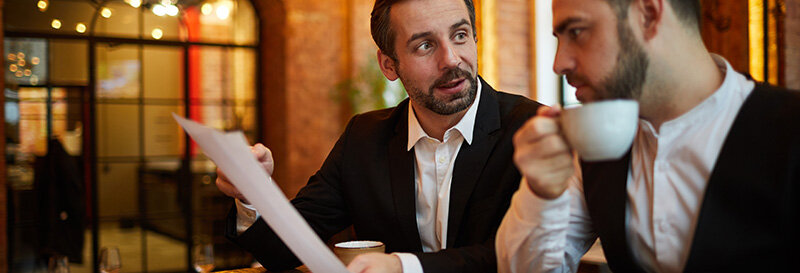 Two adult siblings sitting together in conversation in a restaurant, one with coffee cup