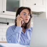 young woman on the phone reviewing a loan modification worksheet at home on her laptop