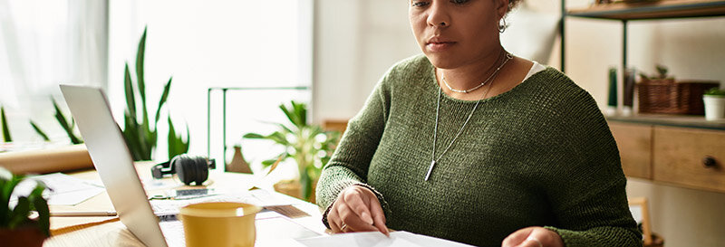 woman studying report at home with laptop on table with coffee and pen