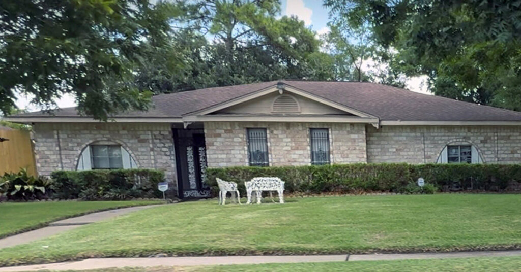 Beige Brick Suburban Ranch House in The Woodlands TX with mowed front yard and cast iron benches