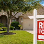 A light brown brick Houston house with landscaped front yard and arch windows and portal to front porch and two car garage on a sonny day with rent to own sign in front