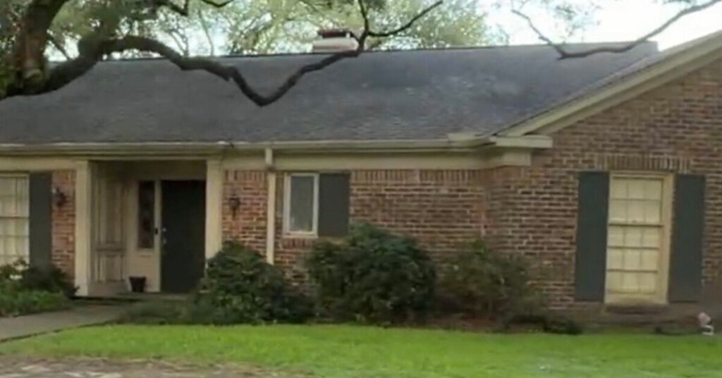 Red Brick Suburban Ranch House in Conroe TX with tree covered and black shutters on sunny day