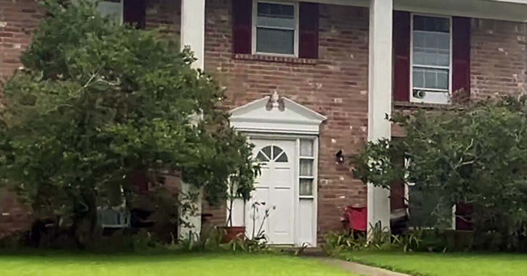 Red Brick two story Suburban Ranch House in Rosenberg TX with two story front porch with large square columns maroon shutters and tall bushes in front
