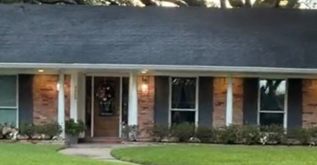 Red and white Brick Suburban Ranch House in Dayton TX with manicured front yard in late afternoon with exterior lighting on and pillar columns on long porch