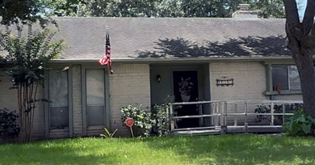 White Brick Suburban Ranch House in Pearland TX with wheelchair ramp flag and blooming bushes