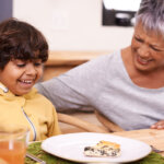 A grandmother and grandchild at a kitchen table together in a well lit kitchen dining room