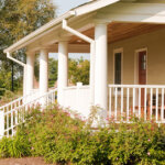 southern style front porch with yellow siding on a sunny day with four Greek columns and white picket railing