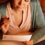 a young woman reads mortgage loan documents at kitchen table during pre-foreclosure