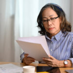 a woman reviews records of her rental property at home with warm light and window in background at table with laptop