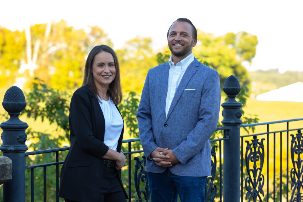 Christie and Grant, the core team behind our company, smiling outside in front of a fence.