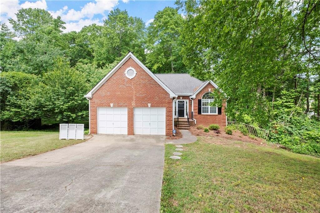 Single-story brick home in Woodstock, Georgia surrounded by lush green trees.