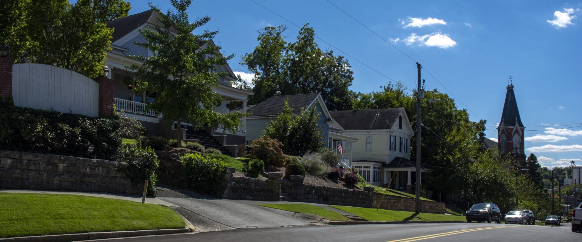 Charming row of houses in downtown Rome, GA, elevated on a hill with a church steeple in the background.