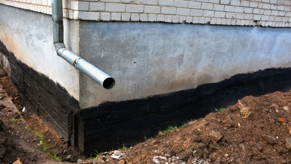 Basement foundation with black waterproofing material applied to the exterior walls to protect against moisture.