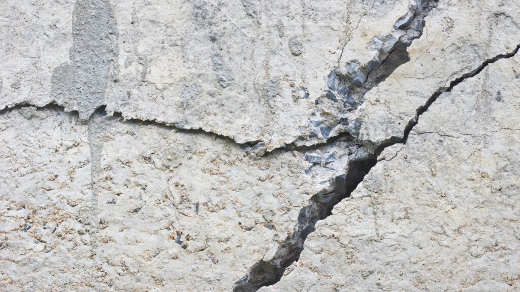 Cracked concrete pavement with visible fractures and uneven surfaces, showing signs of wear and aging.