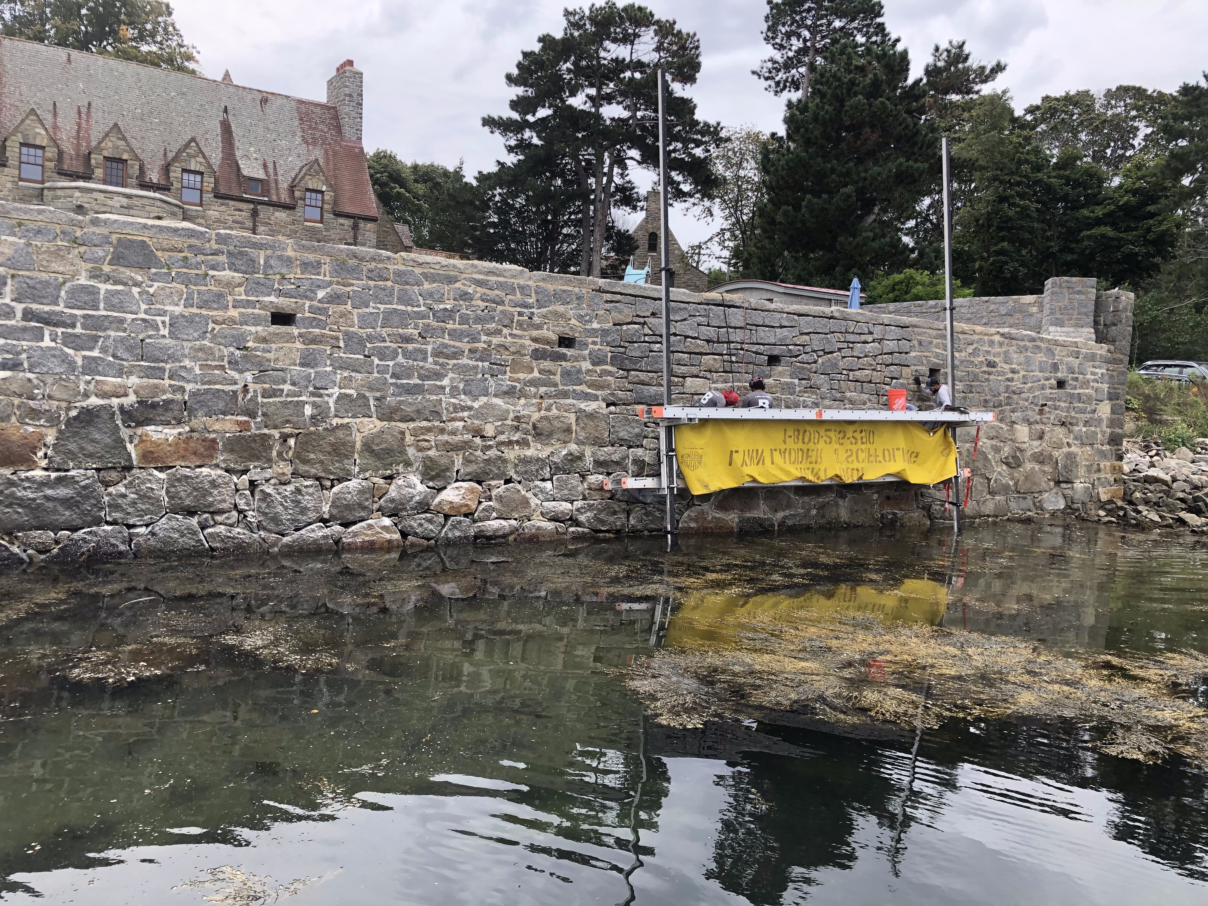 Contractors working on stone wall overlooking water in Boston, MA.