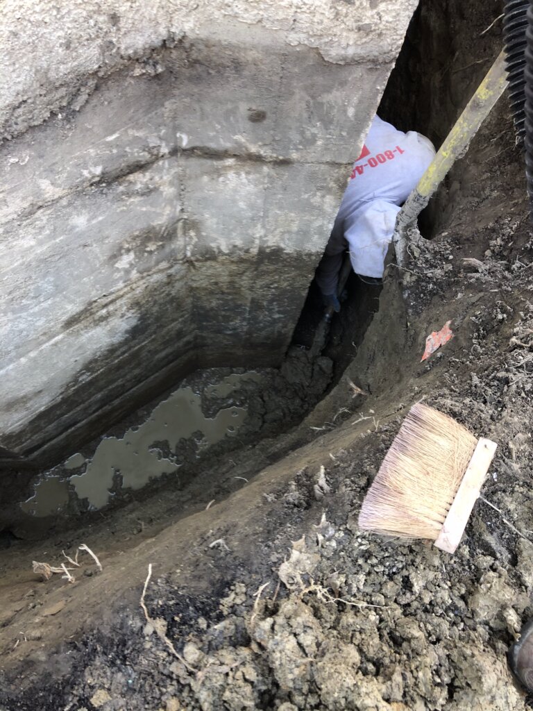 Ground around a house dug up, exposing the foundation in preparation for repair work.