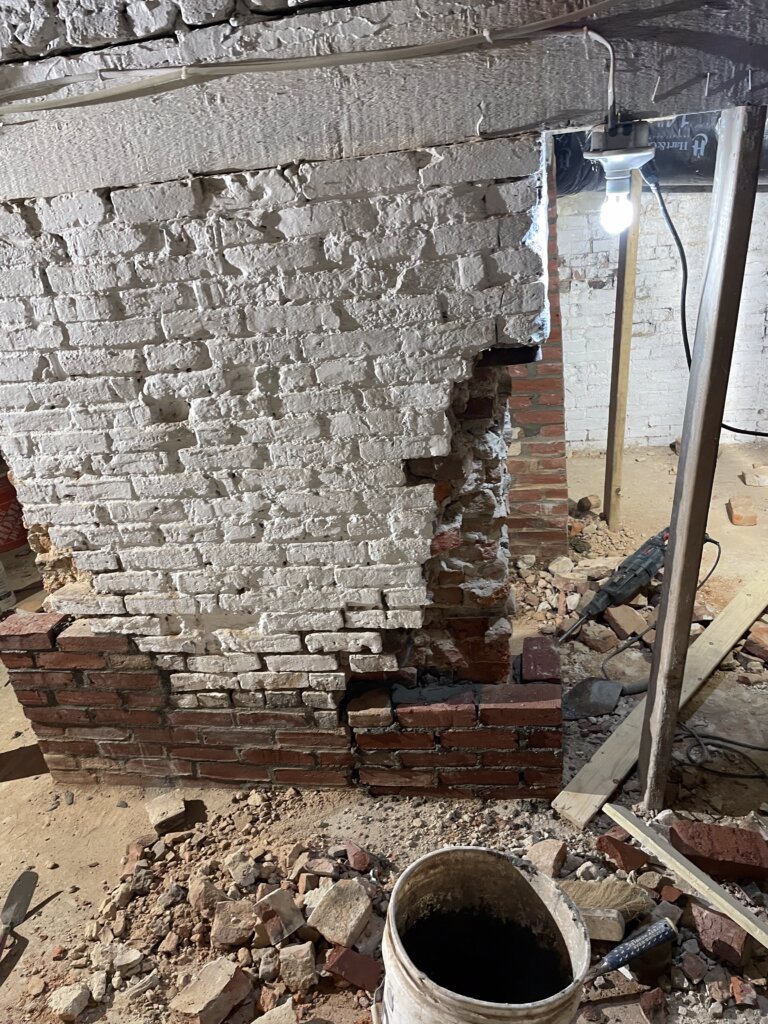 Basement foundation arch with crumbling, weathered brick and no paint, showing signs of age and deterioration before restoration.