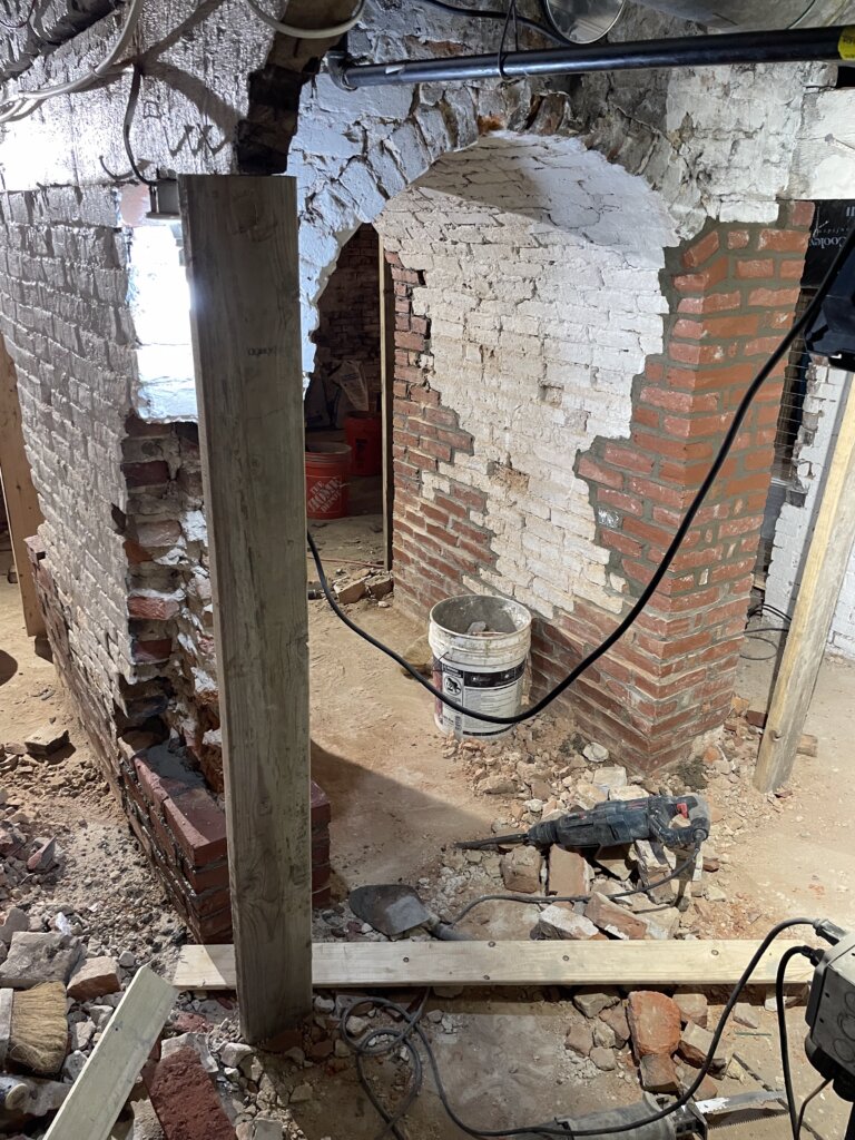 Basement foundation arch with crumbling, weathered brick and no paint, showing signs of age and deterioration before restoration.