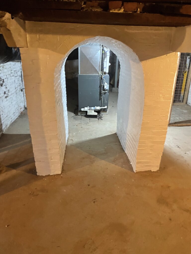 Basement foundation arch featuring newly laid brick and fresh white paint, highlighting recent restoration work.