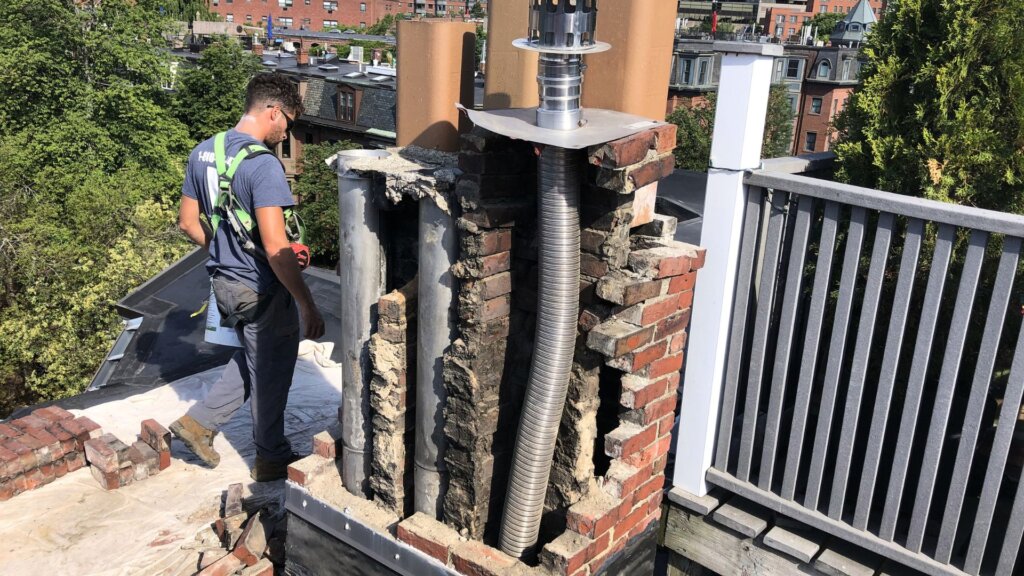 Masonry contractor rebuilding a deteriorated brick chimney on a Boston, MA rooftop