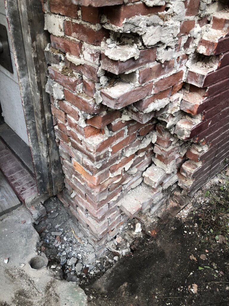 Close-up of a damaged brick foundation wall undergoing repair