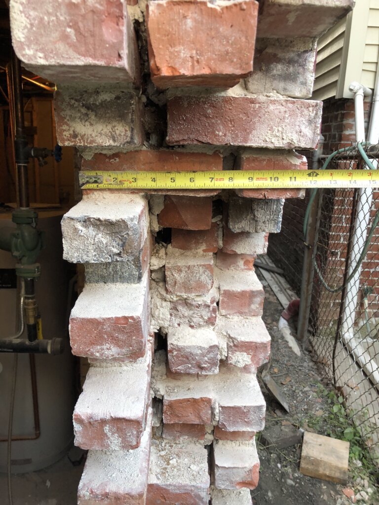 Contractor measuring a damaged brick foundation wall during demolition and repair work