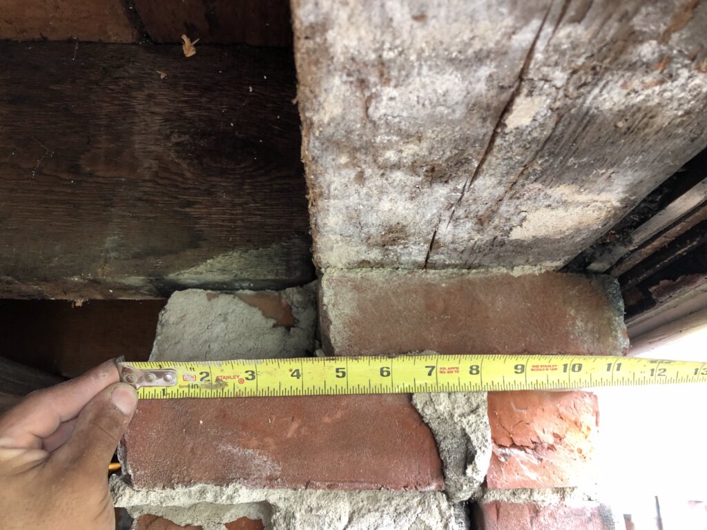Contractor measuring a damaged brick foundation wall during demolition and repair work