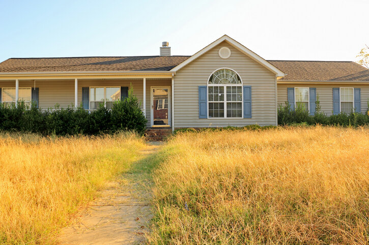 Ranch style single family vacant foreclosure house in Pensacola Florida with tall yellow overgrown grass.