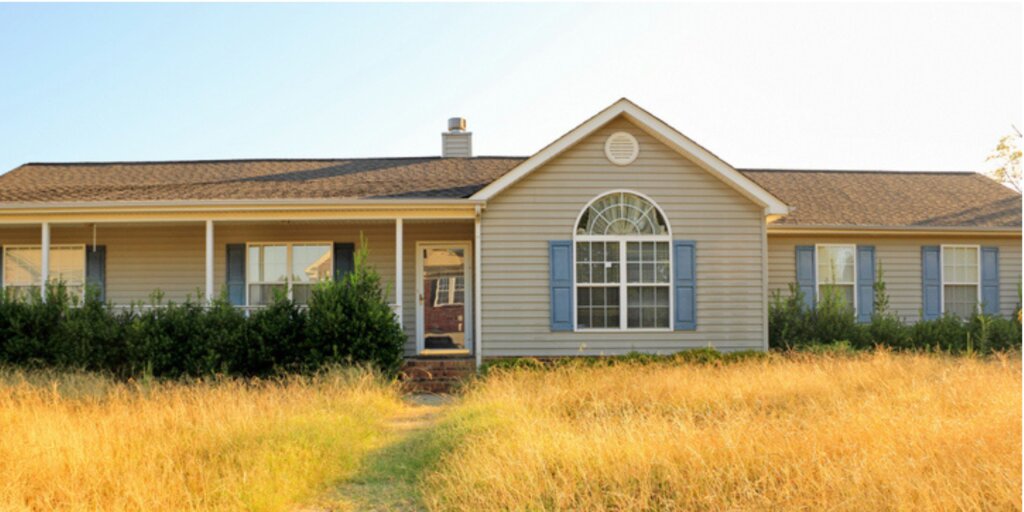 Ranch style single family vacant foreclosure house in Pensacola Florida with tall yellow overgrown grass.