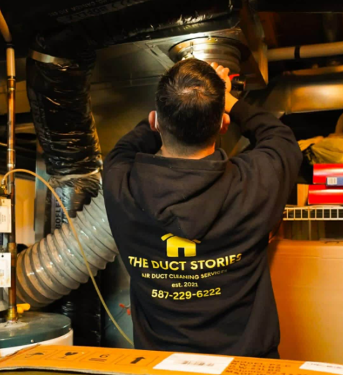 The Duct Stories technician in branded hoodie working on HVAC furnace unit during professional duct cleaning service in Chestermere AB