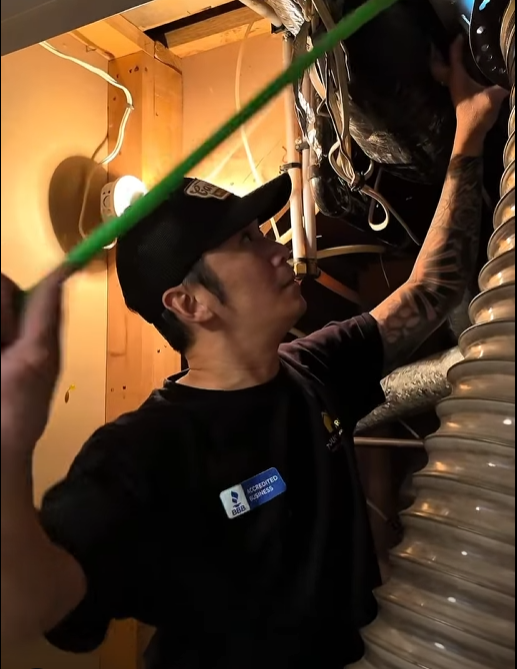 The Duct Stories technician in black cap inspecting interior ductwork and flexible duct hose in a Chestermere home