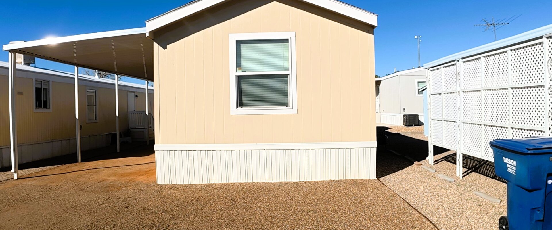 Single wide mobile home in Tucson community with covered carport and gravel yard