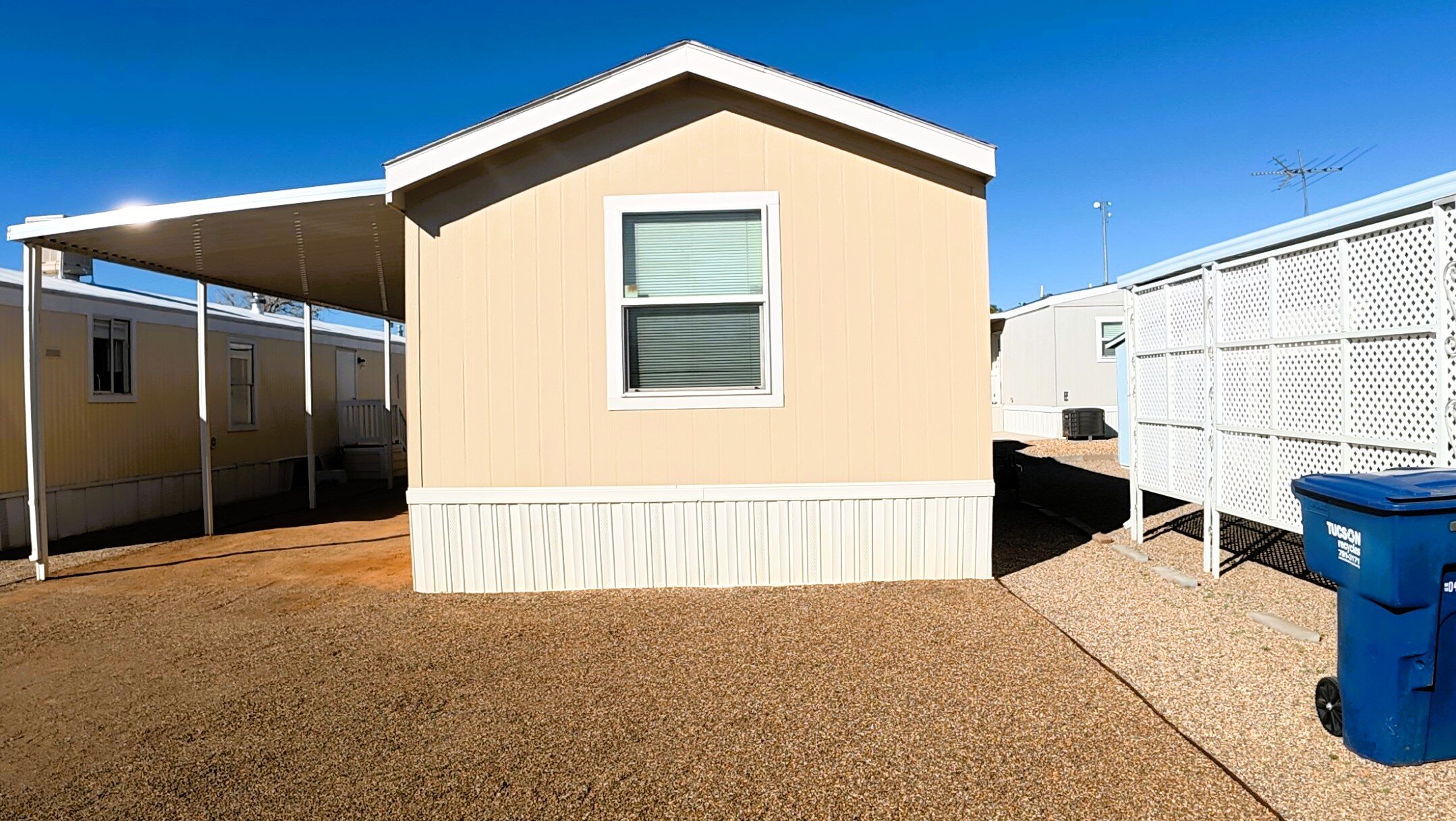 Single wide mobile home in Tucson community with covered carport and gravel yard