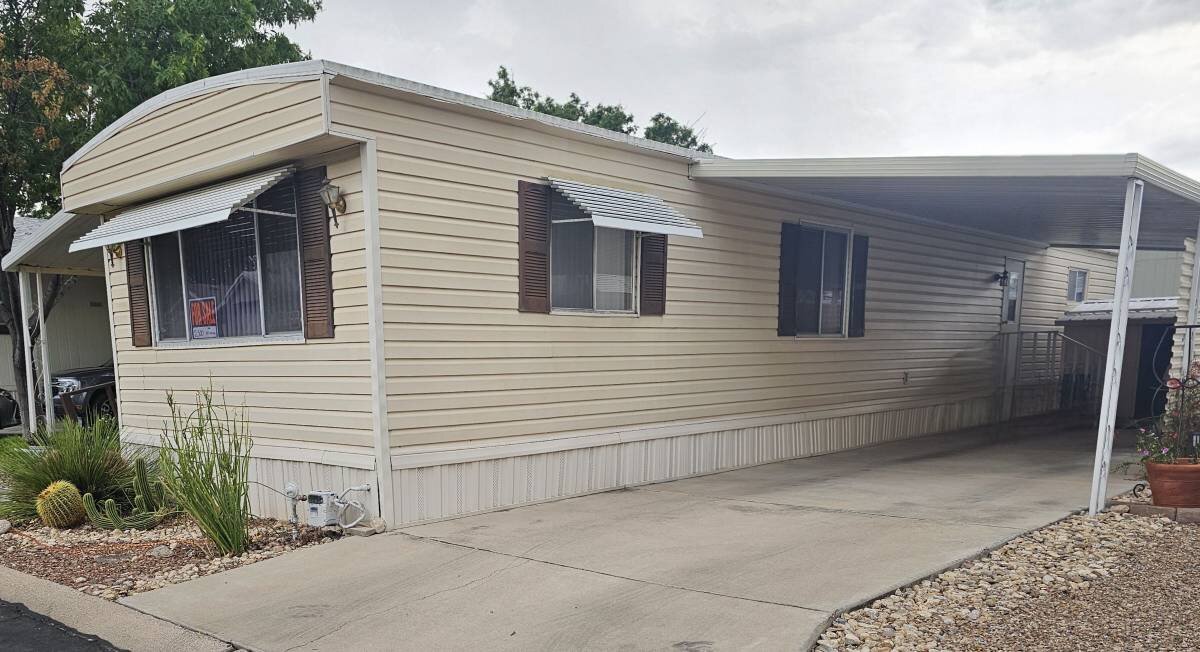 Single wide mobile home in Tucson park with covered carport and concrete driveway
