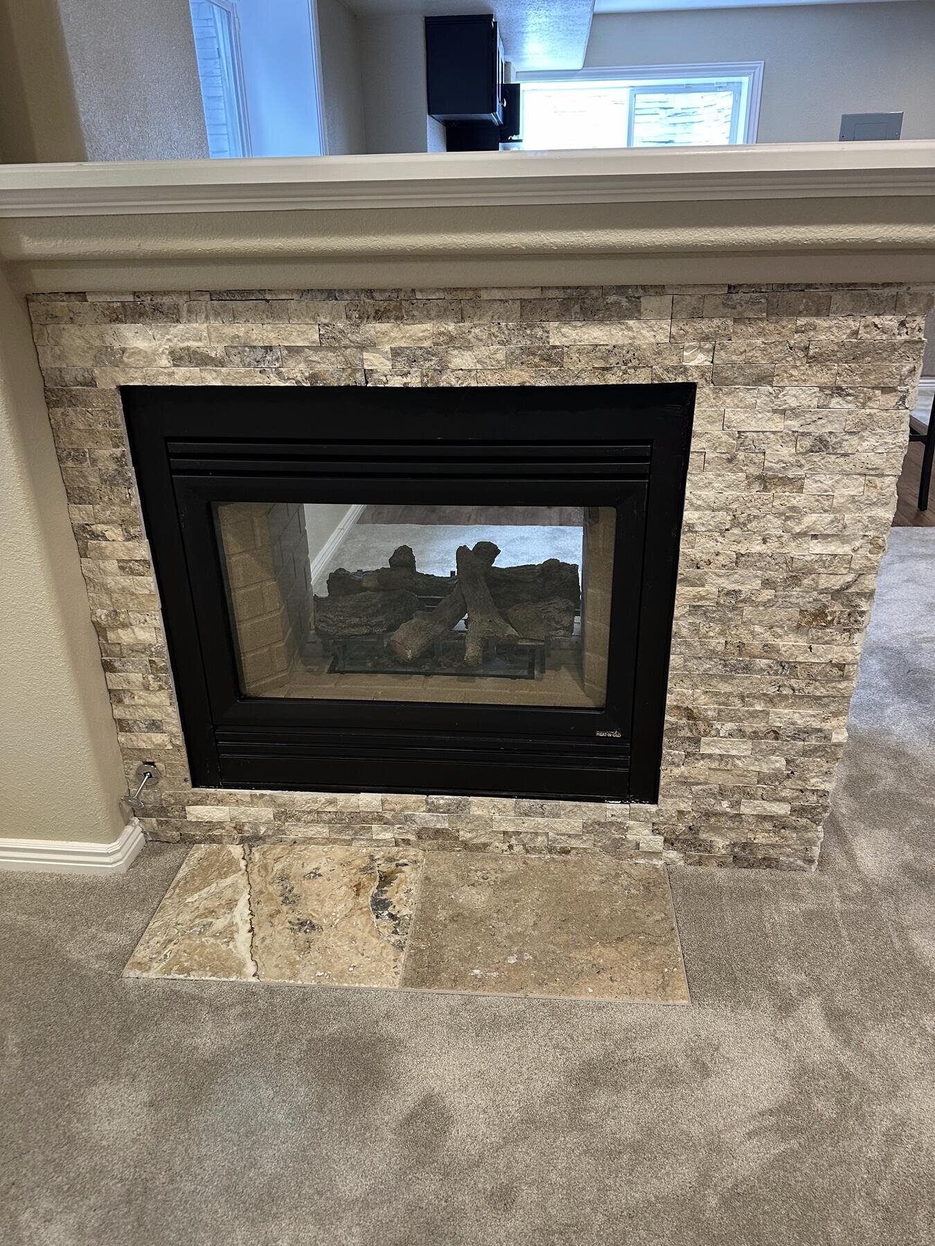 Close detail of a double-sided stone fireplace in a finished basement remodel by The Build Squad