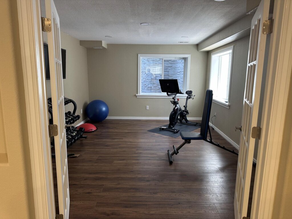 Finished basement home gym with wood flooring and French doors