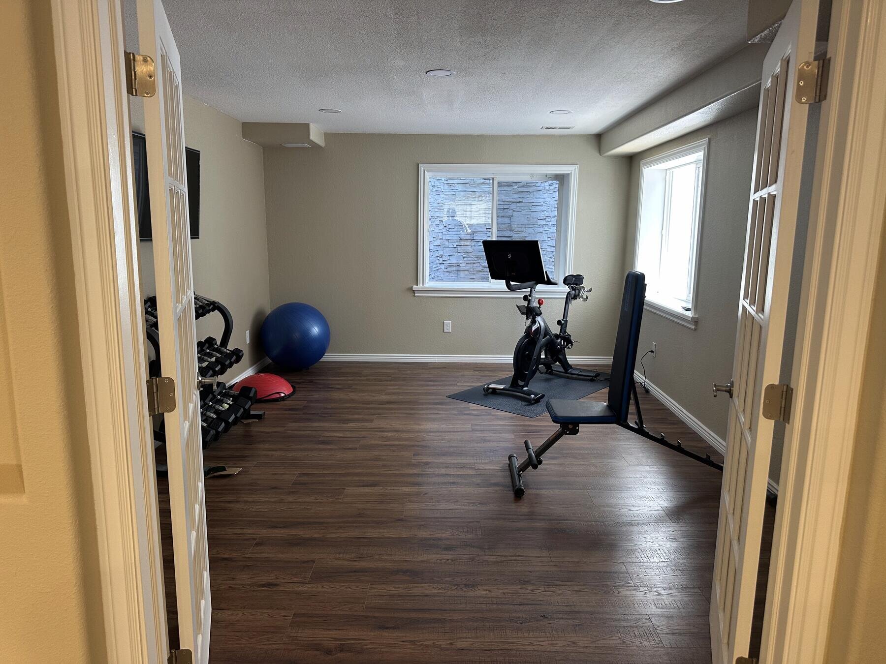 Finished home gym in a remodeled basement with wood flooring and French doors, completed project by The Build Squad